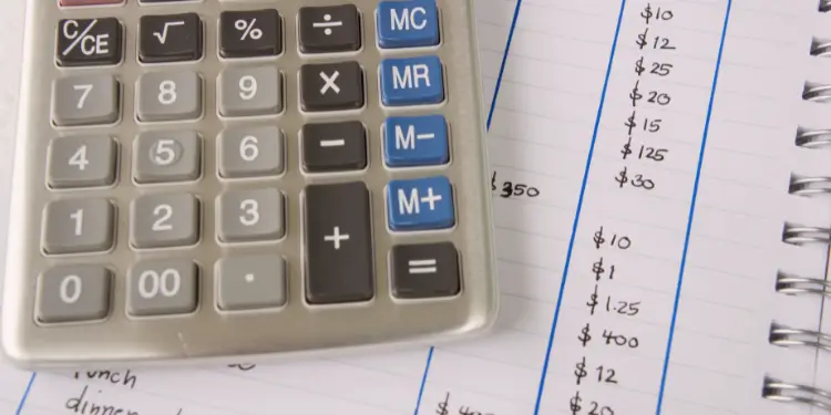 Close-up of a calculator on an open notebook listing handwritten savings categories and amounts.