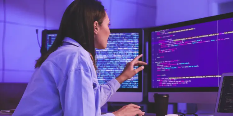 Person seated at multiple screens typing code to represent consistent daily coding practice.