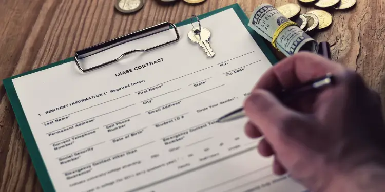Close-up of lease agreement on clipboard, house keys, and cash on wooden table.