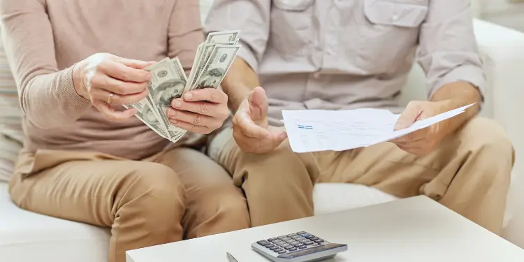 Two partners sit side by side, sorting dollar bills and examining a paper statement with a calculator.
