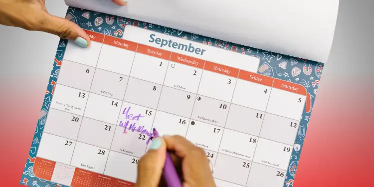 Hand writing on a calendar page to note paydays, bills, and irregular expenses