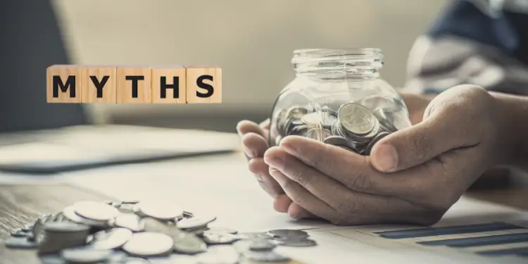 Jar of coins held by hands alongside wooden ‘MYTHS’ blocks and loose change.