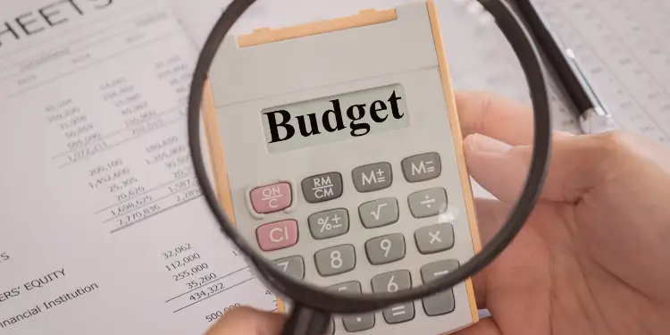 Close-up of a calculator displaying ‘Budget’ over financial sheets with a magnifying glass.