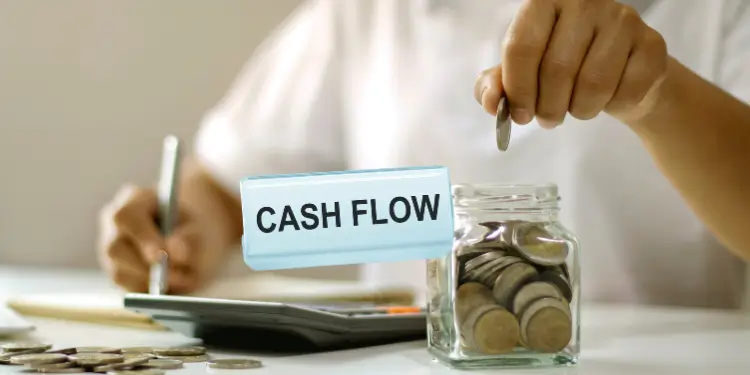 Close-up of coin jar labeled Cash FLOW alongside calculator and financial notes.