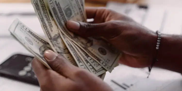Two hands fanning and counting dollar bills to represent setting up automated transfers every payday.