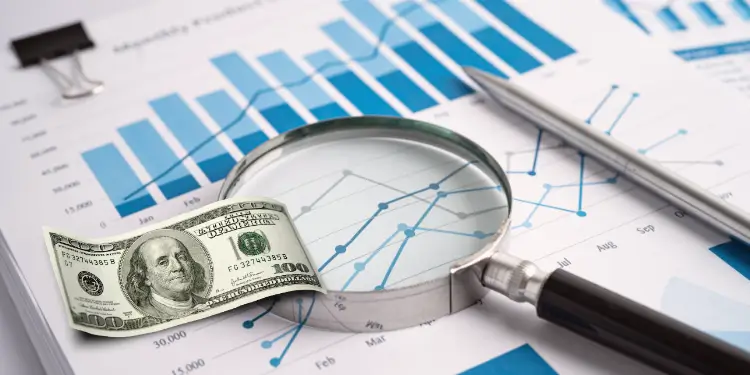Close-up of magnifying glass, money, and financial charts showing income variance.
