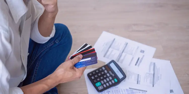 Hand holding credit cards over bills and calculator, symbolizing debt crowding out budget for wants.