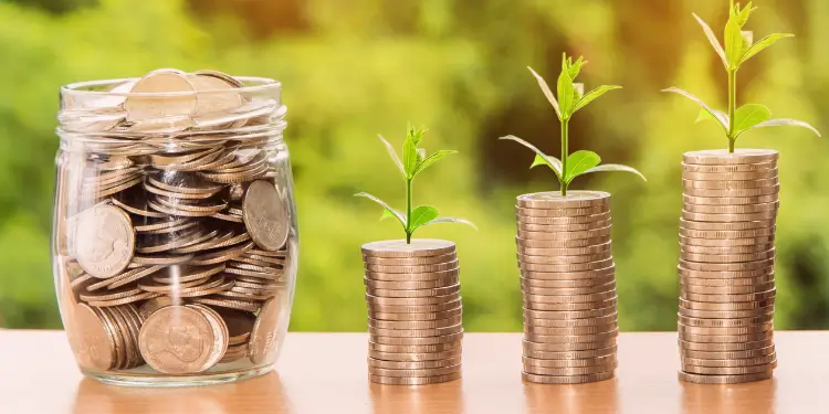 Clear jar of coins next to ascending stacks with small plants growing atop to show savings growth from windfalls.